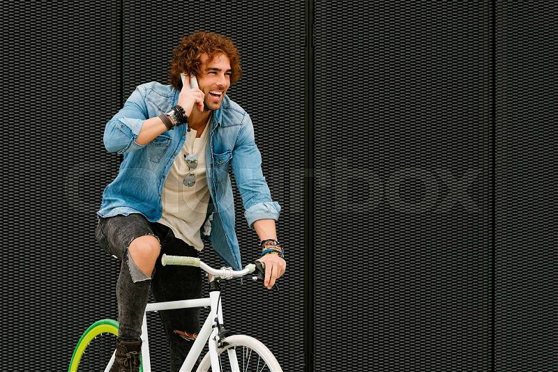Handsome young man with mobile phone and fixed gear bicycle in the street, stock photo