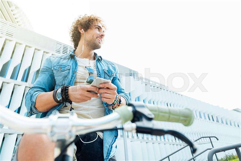 Handsome young man listening music with mobile phone and fixed gear bicycle in the street, stock photo
