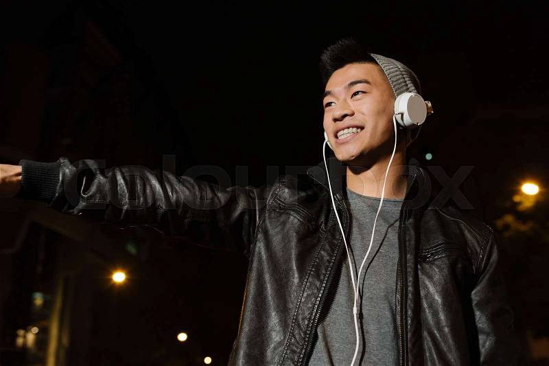Portrait of a asian young man listening music with headphones in the city, stock photo