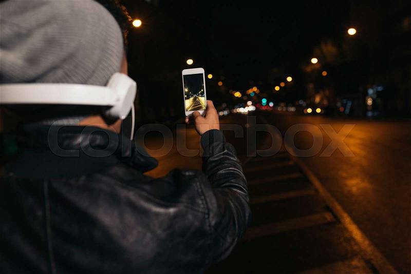 Boy takes a photograph of a street at night, stock photo