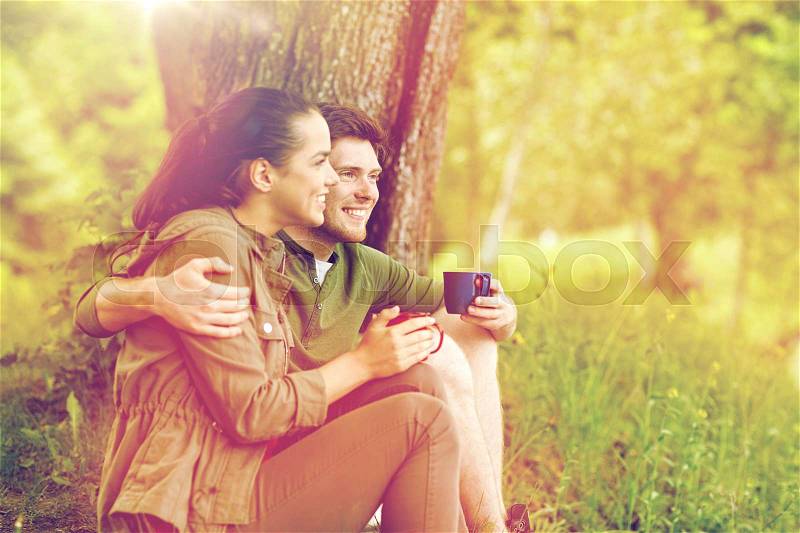 Travel, tourism, hike, camping and people concept - happy couple with cups drinking tea and hugging in nature, stock photo