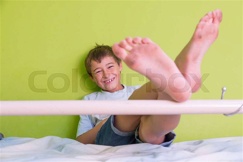 Little kid smiling with dirty feet and sitting at bed, posing on green background close-up, stock photo