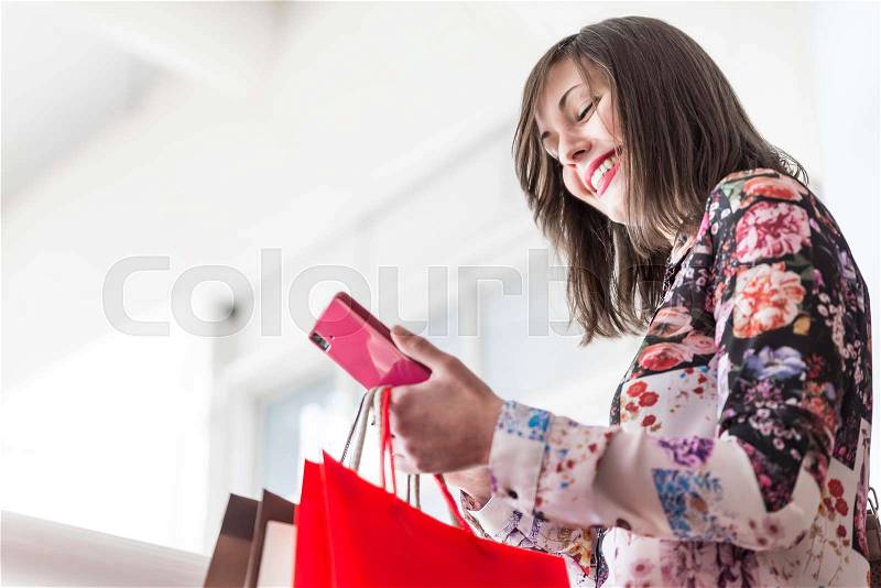 Young woman looking mobile phone, shopping and holding shopping bags, stock photo