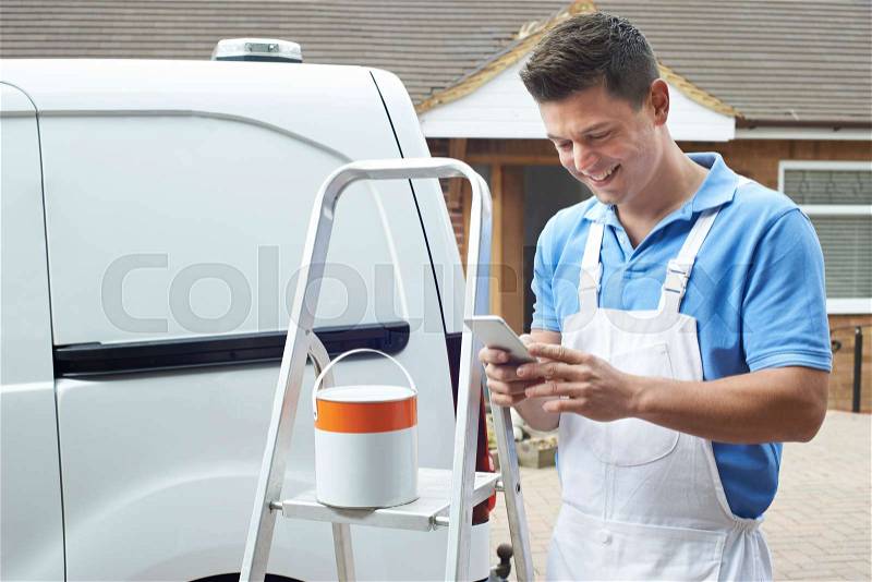 Decorator Using Mobile Phone Standing Outside Domestic Home, stock photo