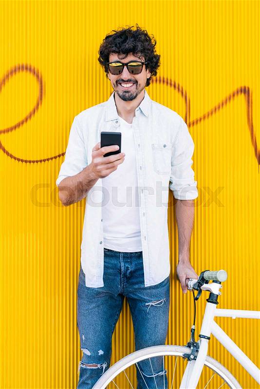 Utdoor portrait of handsome young man with mobile phone and fixed gear bicycle in the street, stock photo