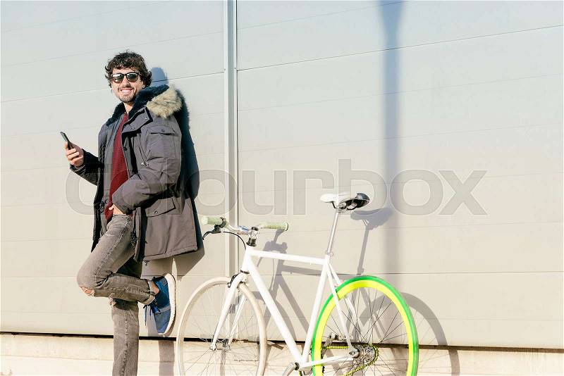 Outdoor portrait of handsome young man with mobile phone and fixed gear bicycle in the street, stock photo