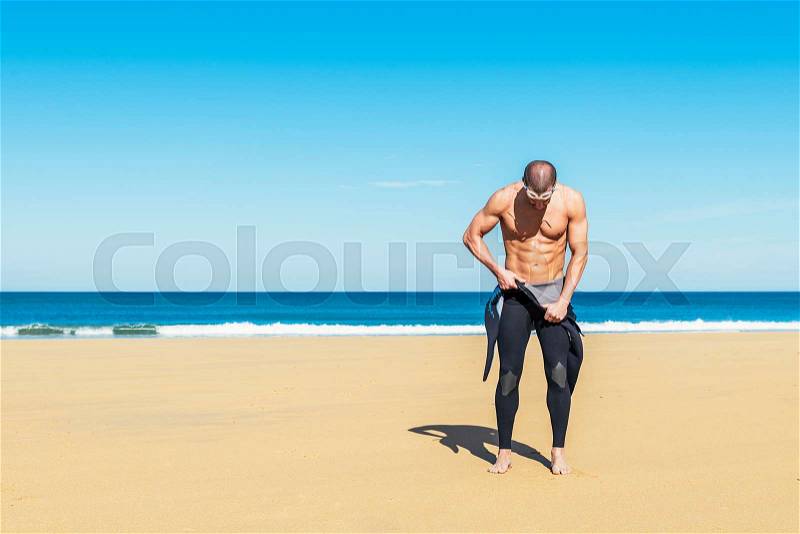 Swimmer putting on his wetsuit on the beach, stock photo