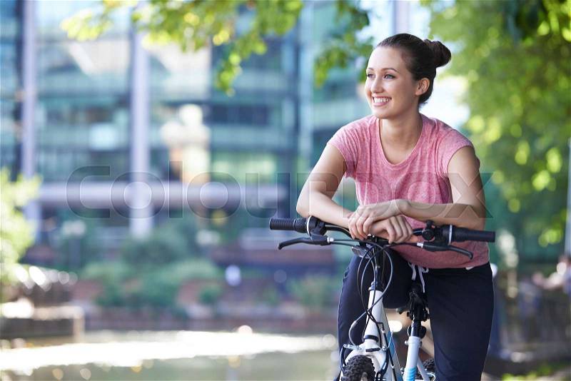 Young Woman Cycling Next To River In Urban Setting, stock photo
