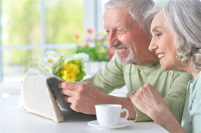 Beautiful old couple reading a newspaper at a table, stock photo