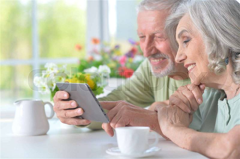 Beautiful old couple with tablet at table, stock photo