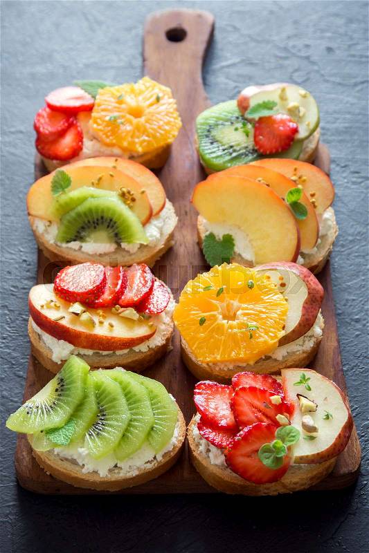 Fruit dessert sandwiches or bruschetta with ricotta cheese. Delicious healthy breakfast toasts with cream cheese, organic fruits and berries, herbs, nuts and bee pollen. Diet healthy food, breakfast, snack, stock photo