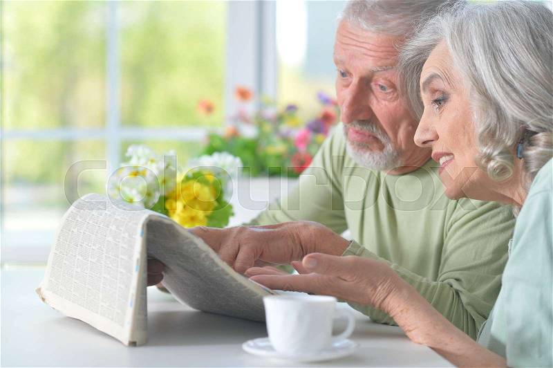 Beautiful old couple reading a newspaper at a table, stock photo