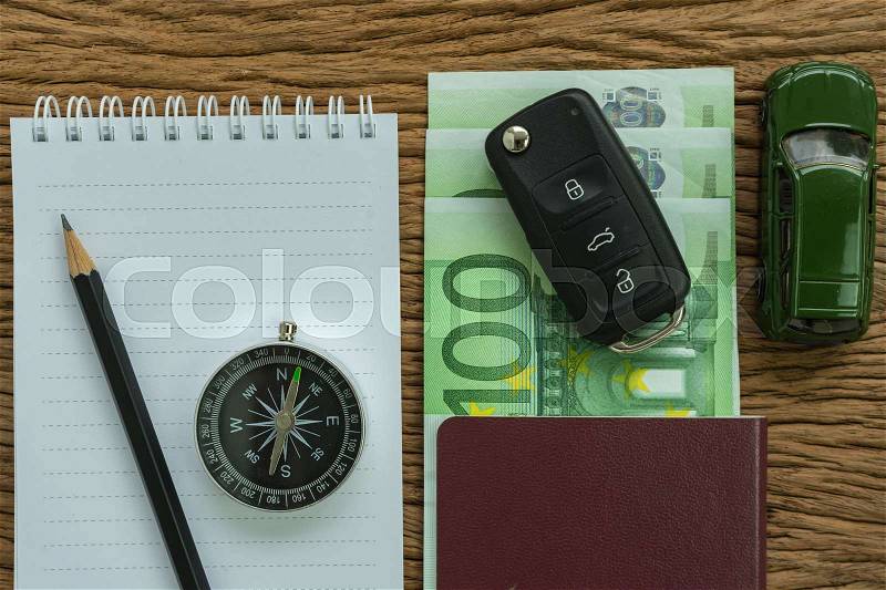 Car key on euro banknotes, passport, compass, pencil, paper note and miniature car on wood table as travel planning road trip concept, stock photo