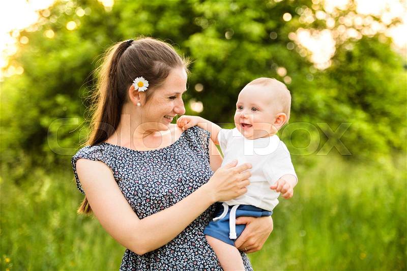 Beautiful young mother in green sunny summer nature holding baby son in the arms, stock photo