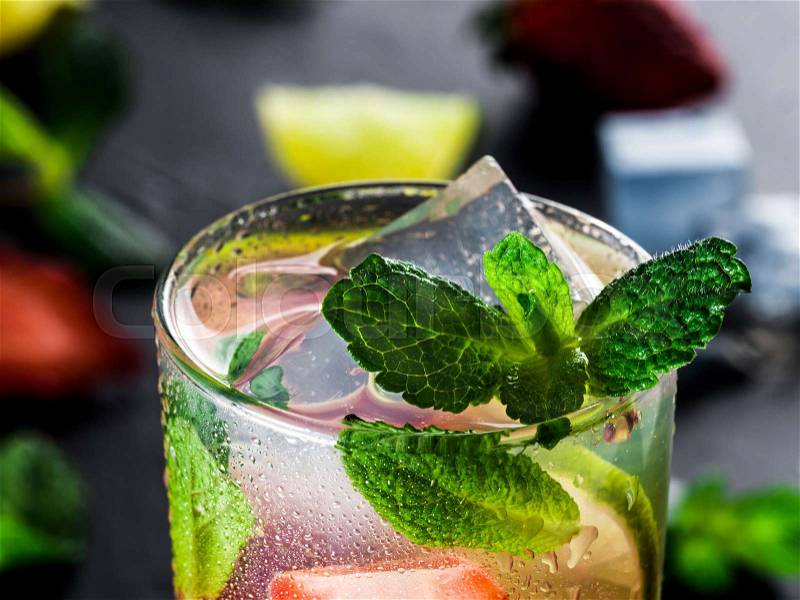 Fresh lemonade with strawberry, lime and mint on dark stone background. Cold summer strawberry drink with mint and ice. Strawberry mojito in glass and ingredients, stock photo