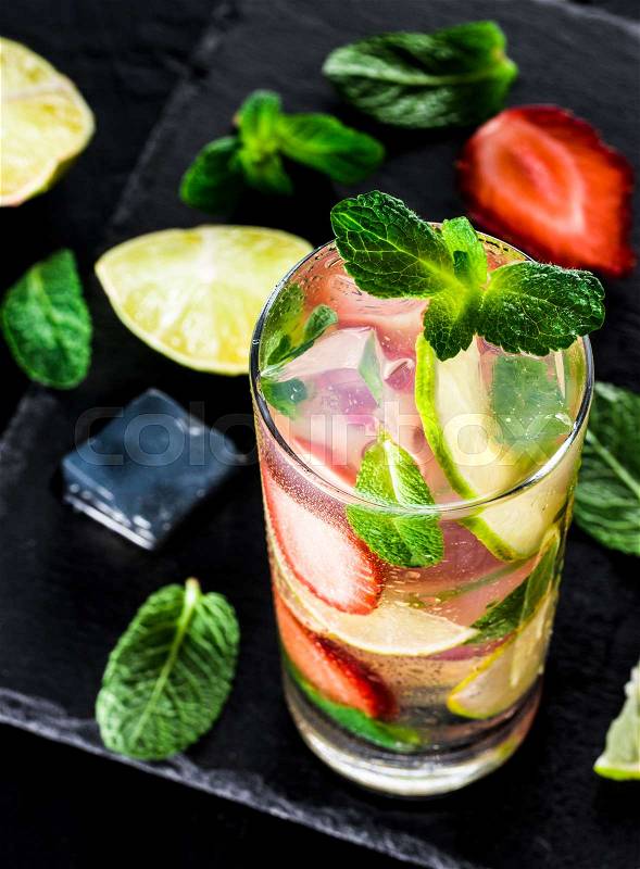 Fresh lemonade with strawberry, lime and mint on dark stone background. Cold summer strawberry drink with mint and ice. Strawberry mojito in glass and ingredients. Vertical, stock photo