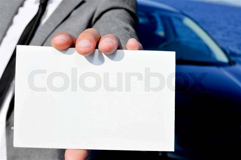 Closeup of a man in suit holding a blank signboard with a car in the background, stock photo