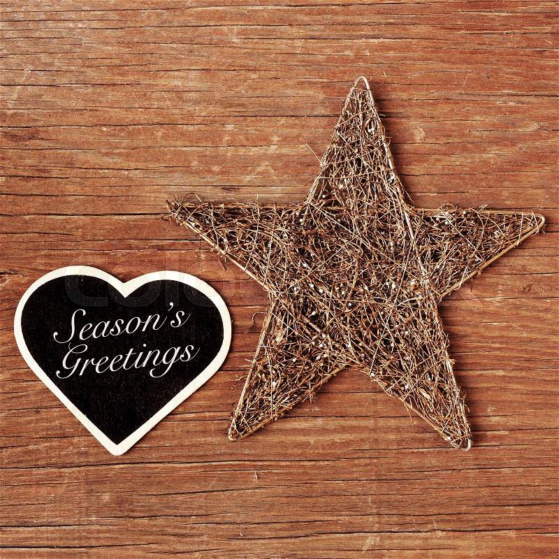 The sentence seasons greetings written in a heart-shaped chalkboard and a rustic christmas star on a wooden surface, stock photo