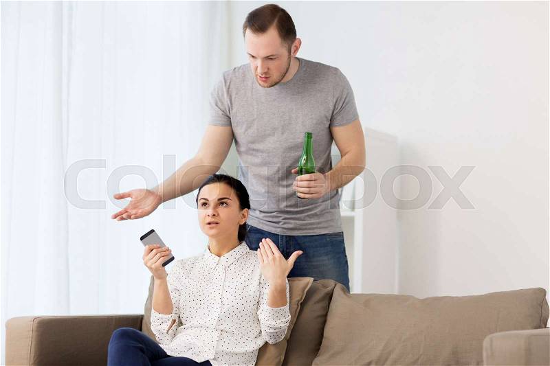 People, relationship difficulties and conflict concept - man drinking beer and woman with smartphone having argument at home, stock photo