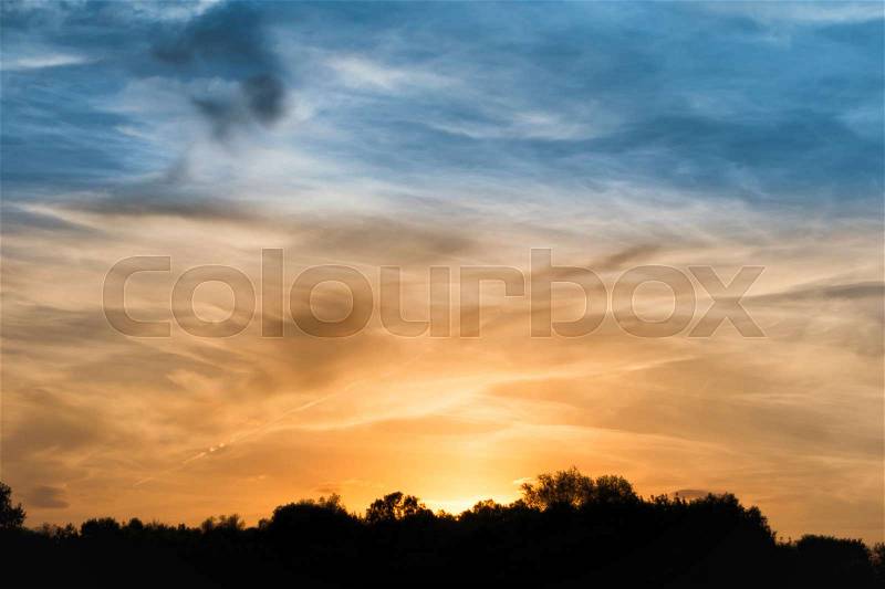 Sunset over forest silhouette. Dramatic sky with sun and clouds, stock photo