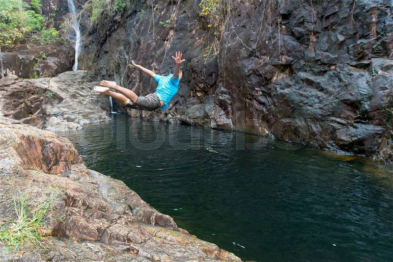 Man jumping on Waterfall in deep rain forest jungle Thailand, stock photo