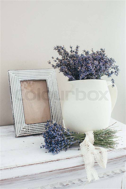 Shabby chic interior decor for farmhouse. Lavender in pitcher and blank photo frame on a vintage shelf over pastel wall. Provence home decoration, stock photo