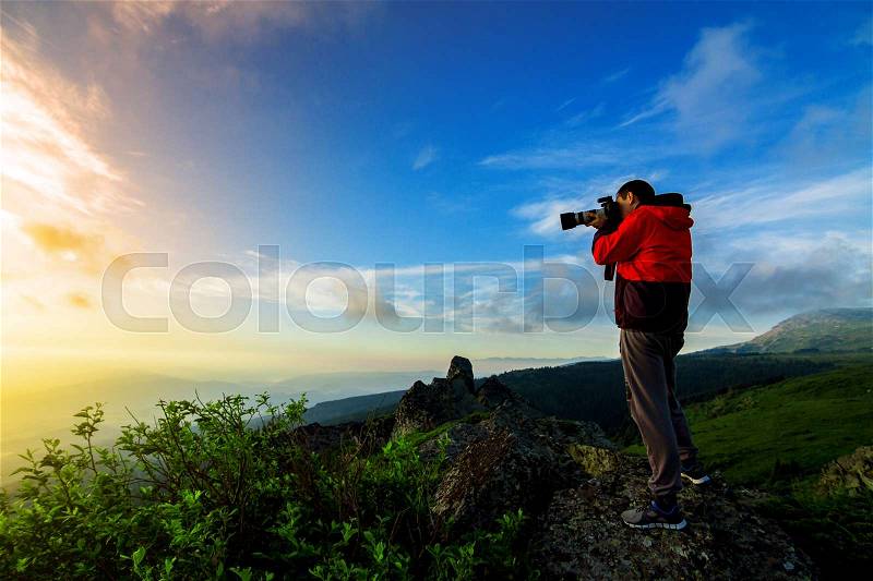 Man on a hill at sunset with camera making photo, stock photo