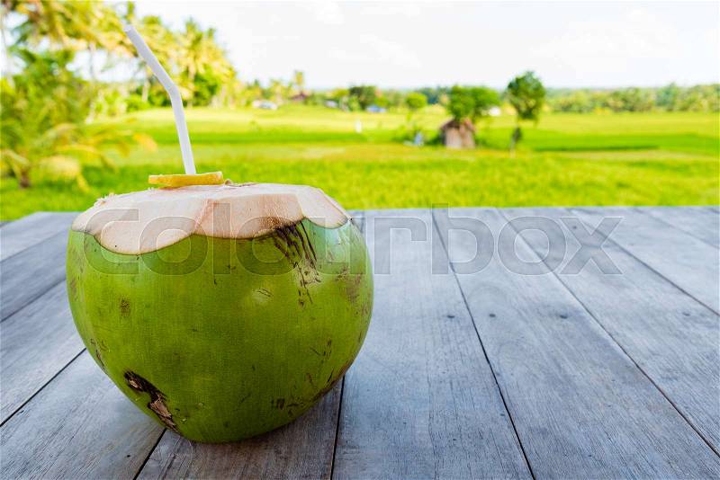 Green young coconut with straw on table, rice fields and coconut trees in backgroud. Copy space available, stock photo