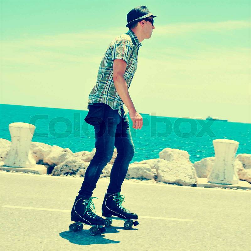 A young man roller skating near the sea, with a cross-processed effect, stock photo