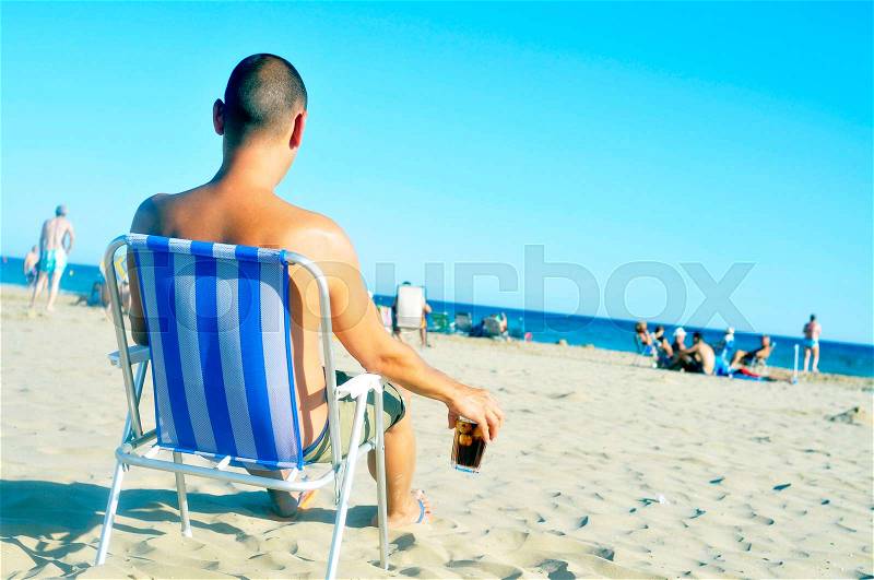 A young man hanging out on the beach, with a glass with cola drink, stock photo