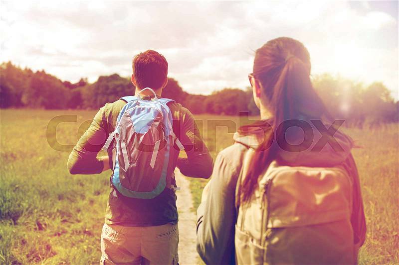 Travel, hiking, backpacking, tourism and people concept - close up of couple with backpacks walking along country road, stock photo