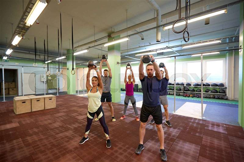 Sport, fitness, weightlifting and training concept - group of people with kettlebells and heart-rate trackers exercising in gym, stock photo