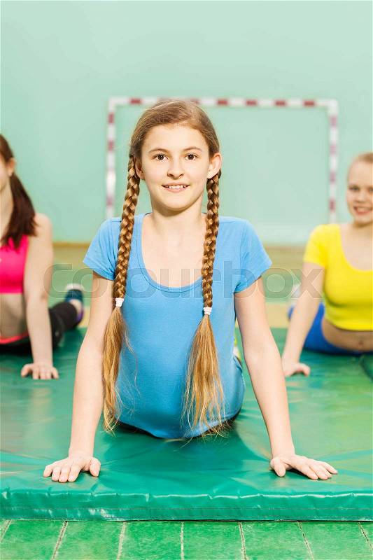 Portrait of happy teenage blond girl stretching her back during gymnastic class in gymnasium, stock photo