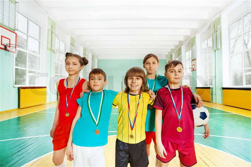 Portrait of happy football winners, preteen boys and girls, standing with medals in sports hall, stock photo