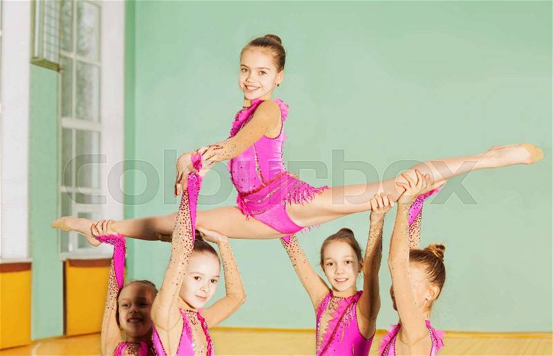 Group of beautiful preteen girls performing rhythmic gymnastics element in sports hall, stock photo