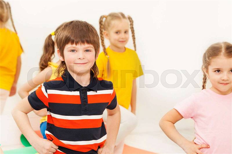 Portrait of happy kid boy kneeling with hands on waist, practicing gymnastics in kindergarten, stock photo