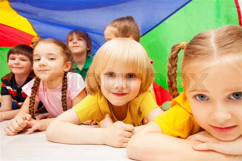 Close-up portrait of happy preschool children laying on the floor under the tent made of rainbow parachute, stock photo