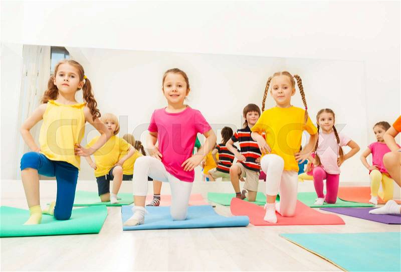 Portrait of happy little girls standing on knee in line during gymnastics lesson in fitness class, stock photo