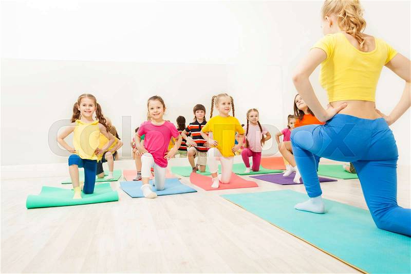 Group of happy kids doing exercises in gym with female gymnastics coach, stock photo