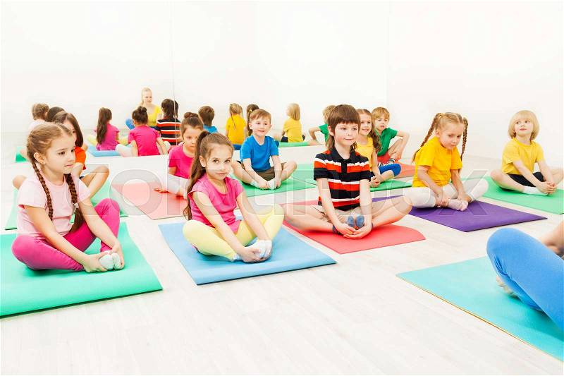Portrait of 5-6 years old boys and girls doing butterfly exercise sitting on yoga mats in gym, stock photo