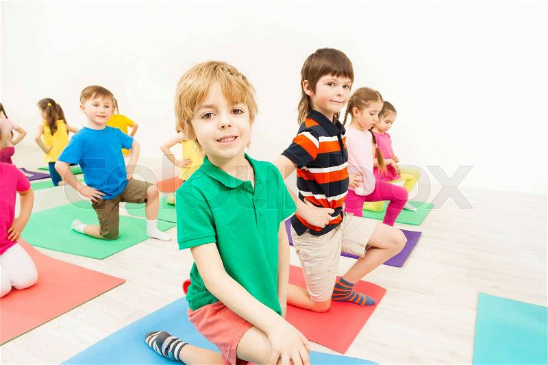 Portrait of happy kids practicing gymnastics, doing knee bending exercises on mats, against blanked background, stock photo