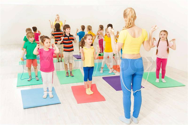Group of 5-6 years old kids jumping on ropes with female gymnastic coach in gym, stock photo
