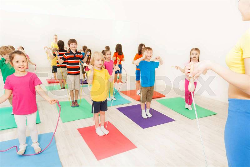 Sports coach teaching kids jumping with skipping rope in gym, stock photo
