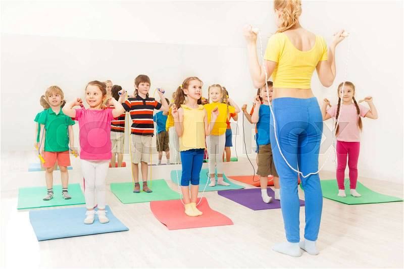 Group of happy kids jumping ropes with sports teacher at gym lesson, stock photo