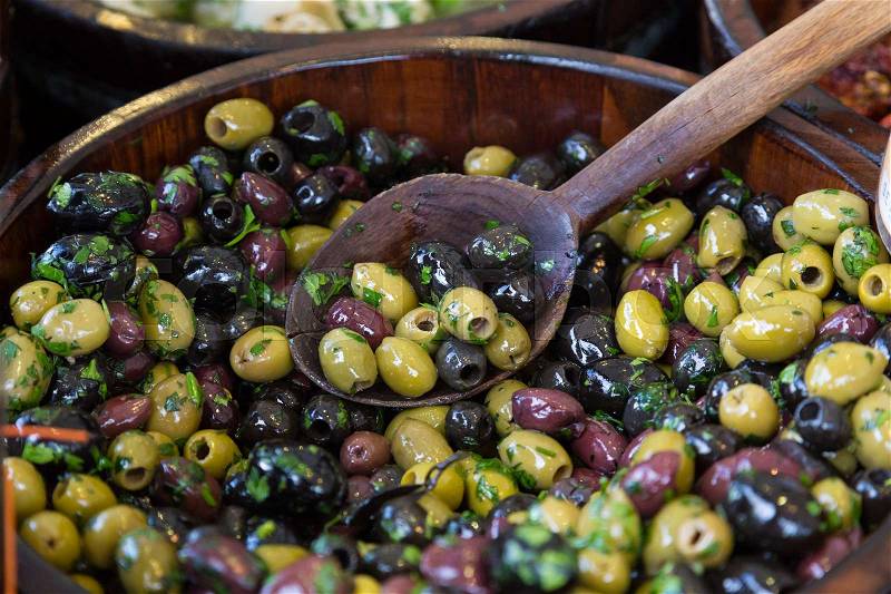 Olives with serving spoons in wooden bowls being sold on local grocery market, stock photo