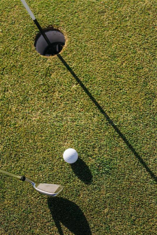 Golf club hitting ball into hole on green grassy field, stock photo