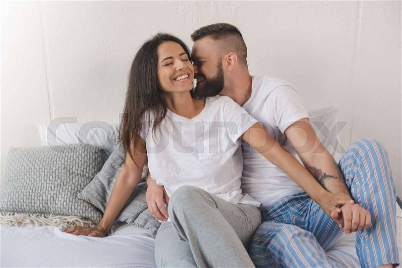 Sensual young couple smiling and embracing in bed at home, stock photo