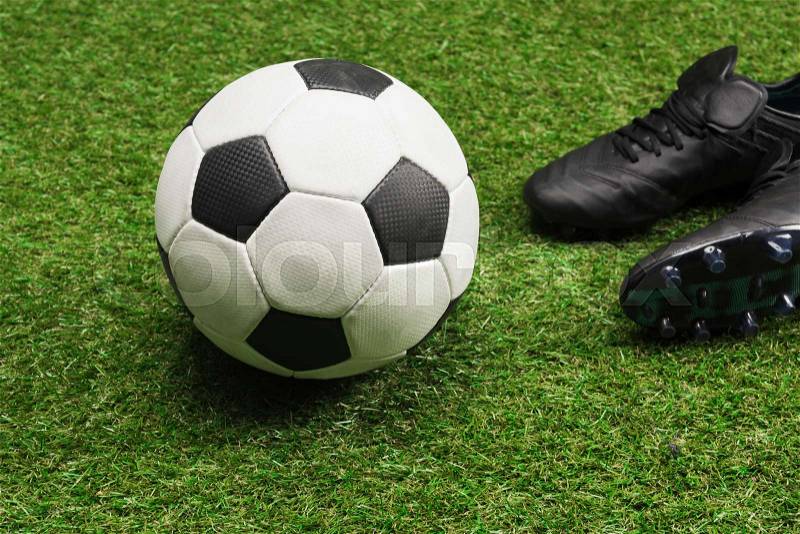 Close-up of soccer ball with pair of black sports shoes on grass, stock photo