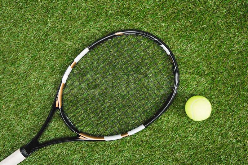 Top view of tennis racket and ball lying on green lawn, stock photo