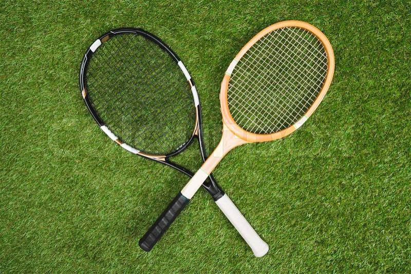 Top view of plastic tennis and wooden badminton rackets on green lawn, stock photo
